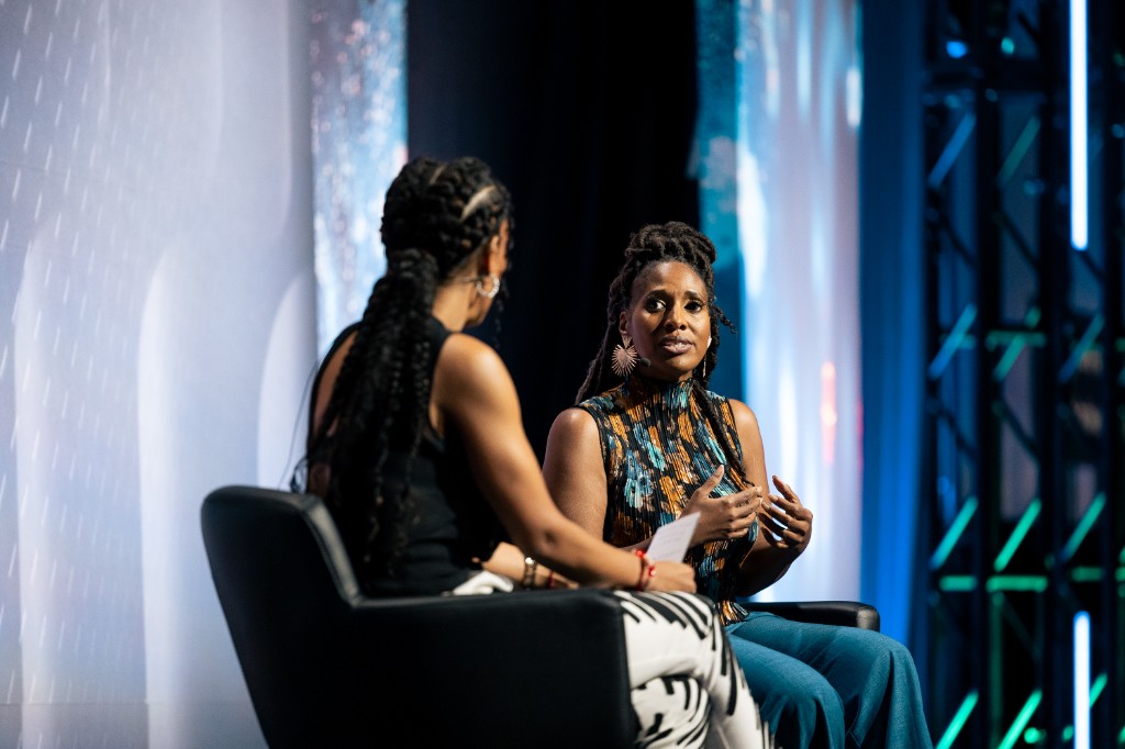 Speakers seated on stage in conversation at AfroTech, one holding notes